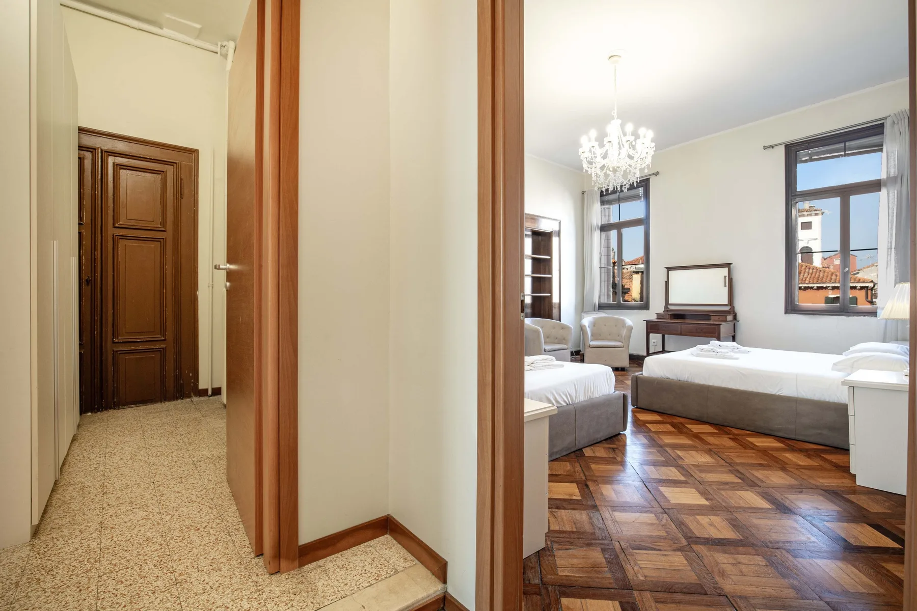 A bedroom with two beds, a chandelier, and parquet flooring.