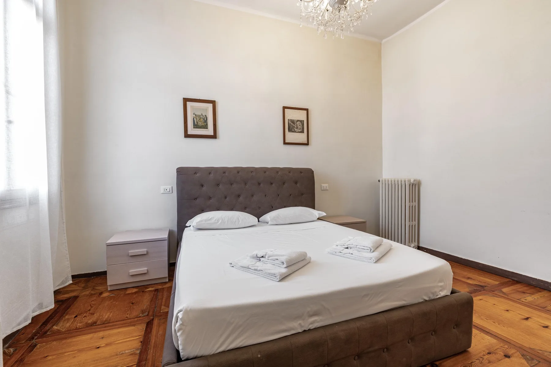 A bedroom with a double bed, bedside tables, and framed pictures above the headboard.
