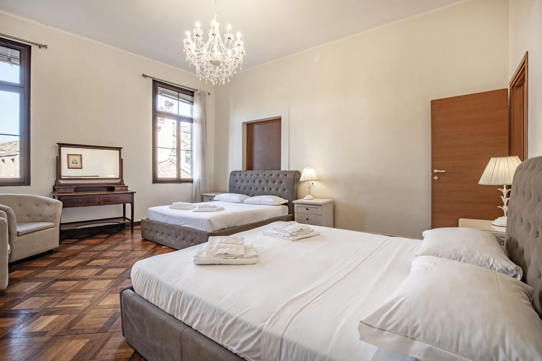 A bedroom with two beds, tall windows, and a chandelier.
