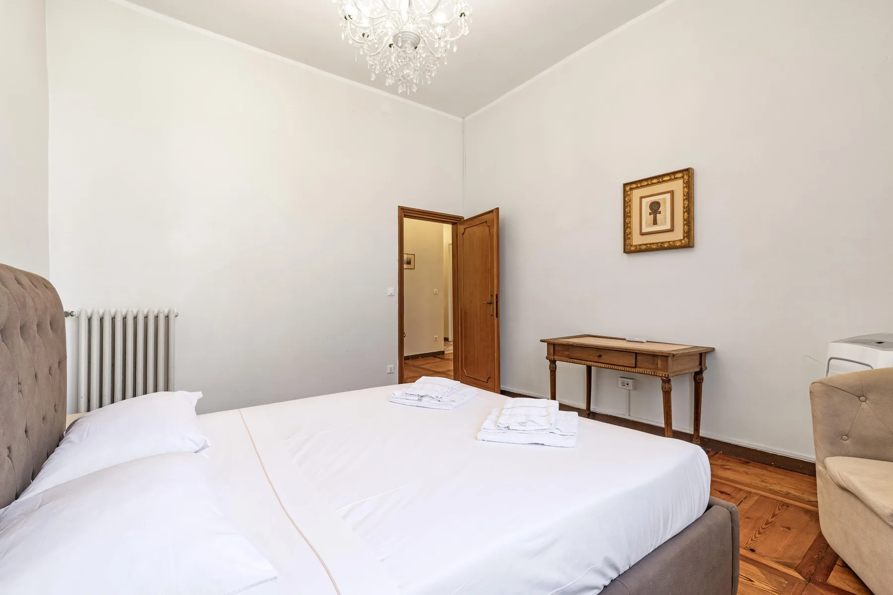 A bright bedroom with a neatly made bed and an open doorway.