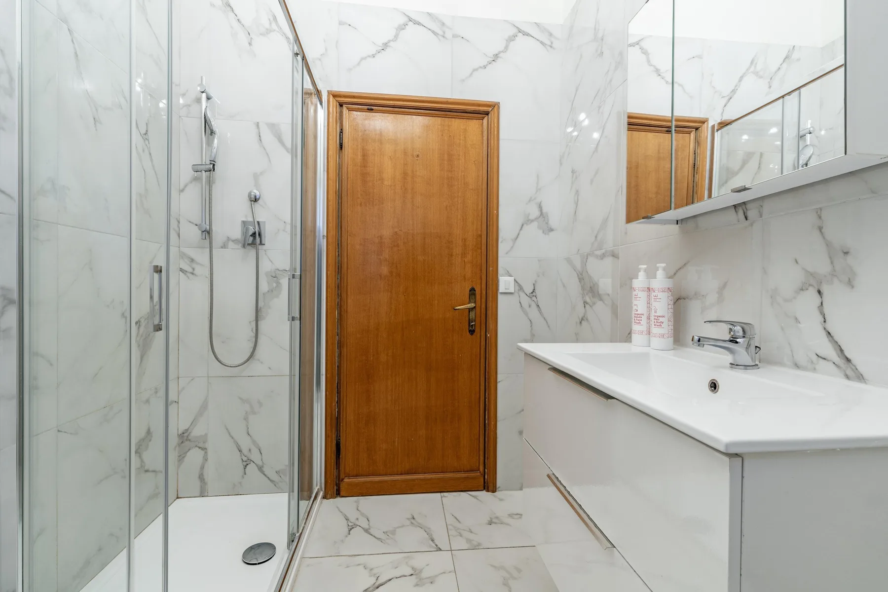 A marble-tiled bathroom with a glass shower and a white sink vanity.