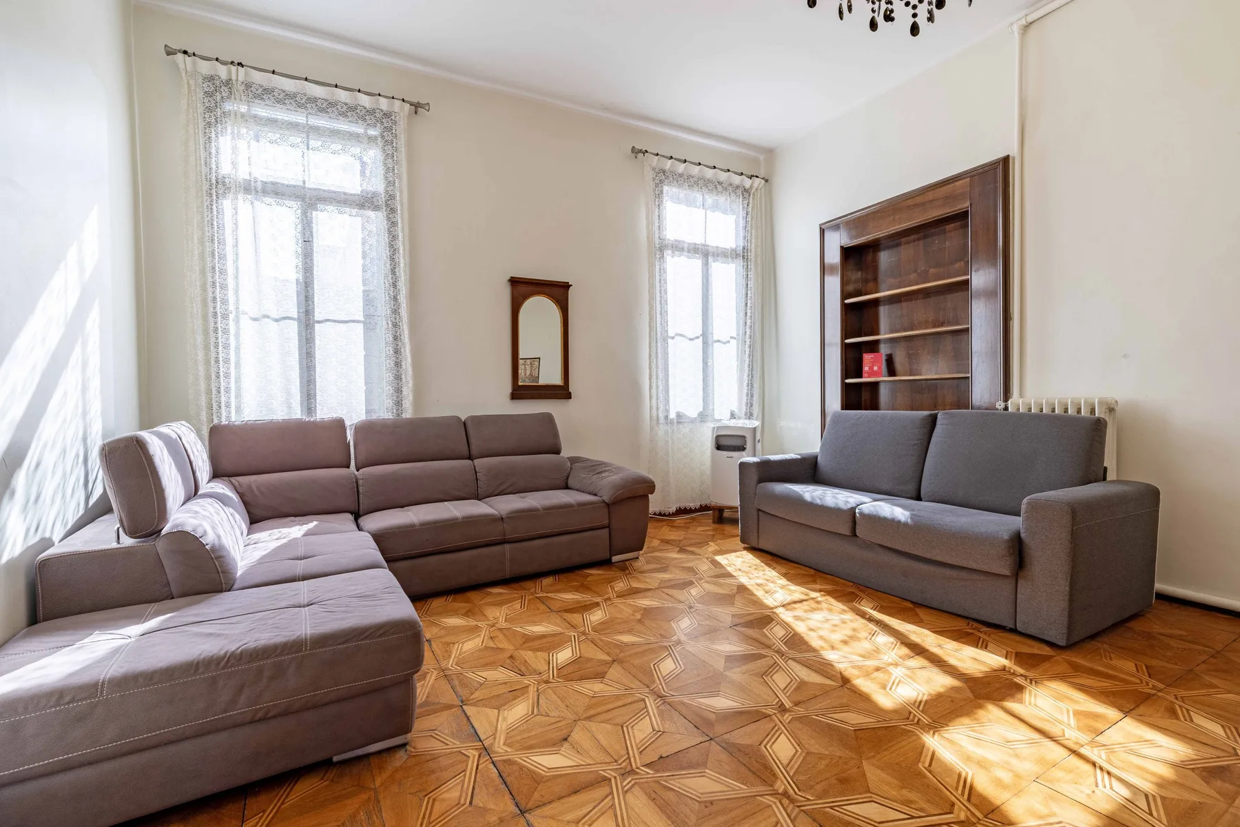 A bright living room with seating, tall windows, and a wooden bookcase.
