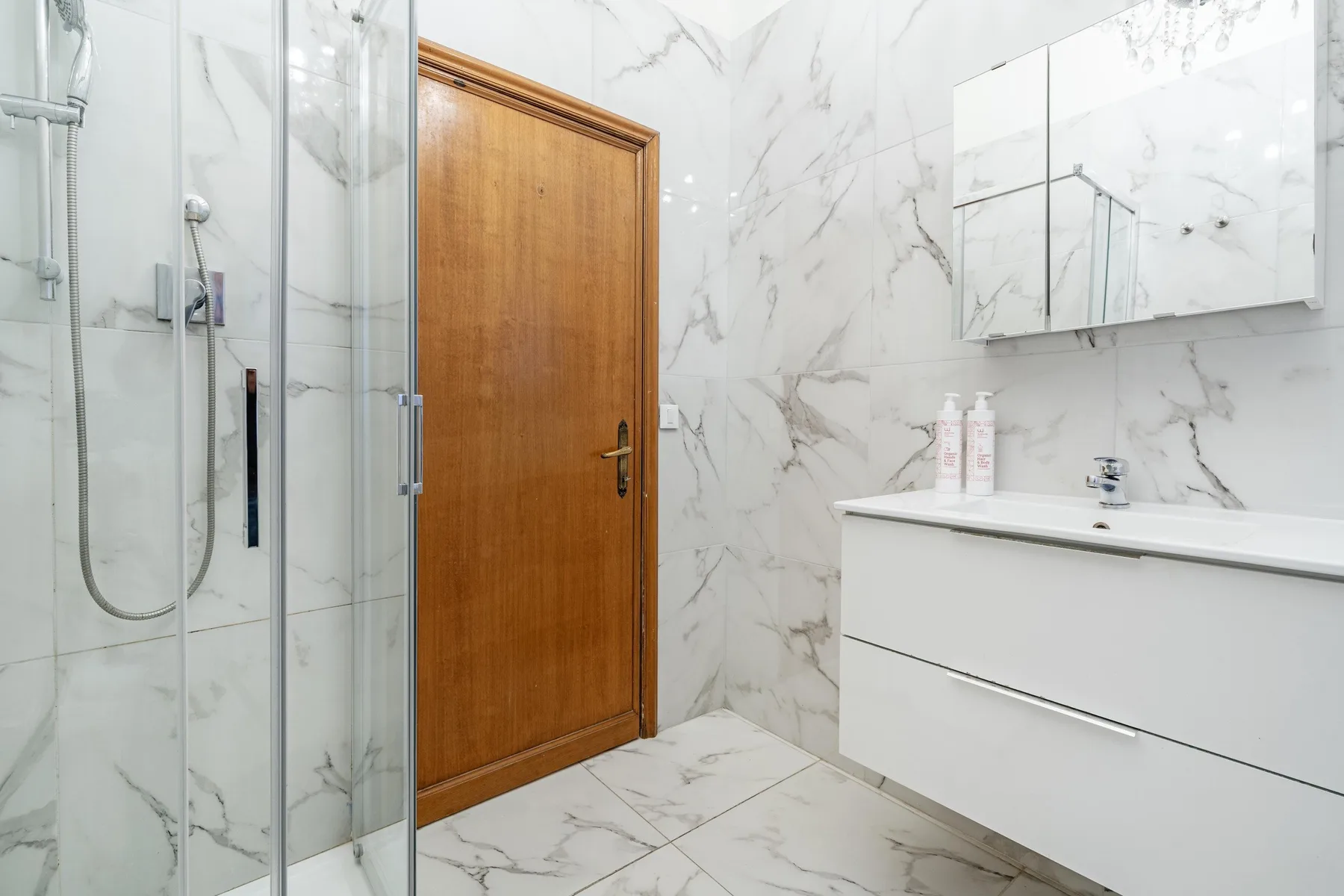 A bright bathroom with a glass shower, wooden door, and white vanity.