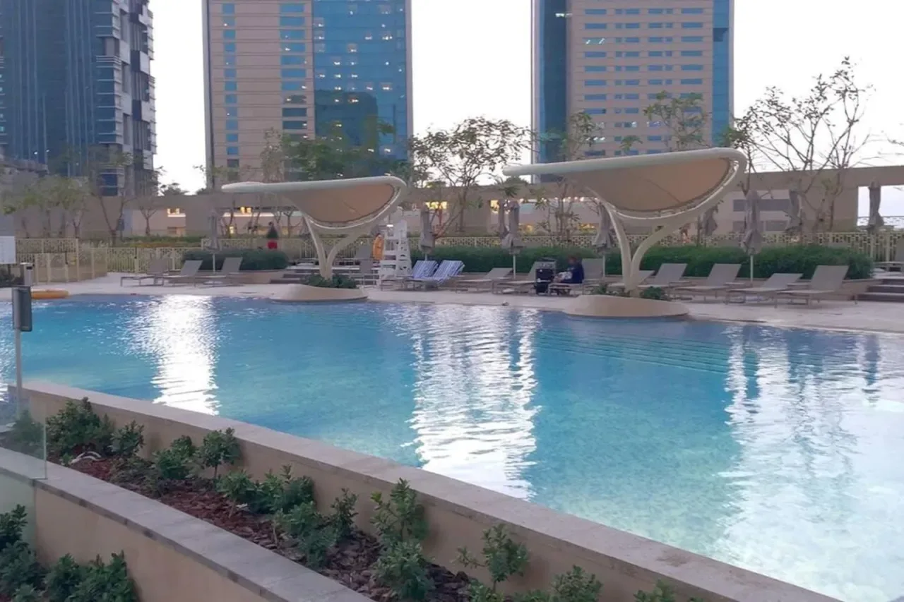 An outdoor swimming pool with lounge seating and tall buildings in the background.