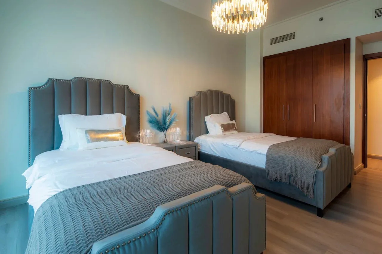 A bedroom with two beds, gray bedding, and a bedside table.