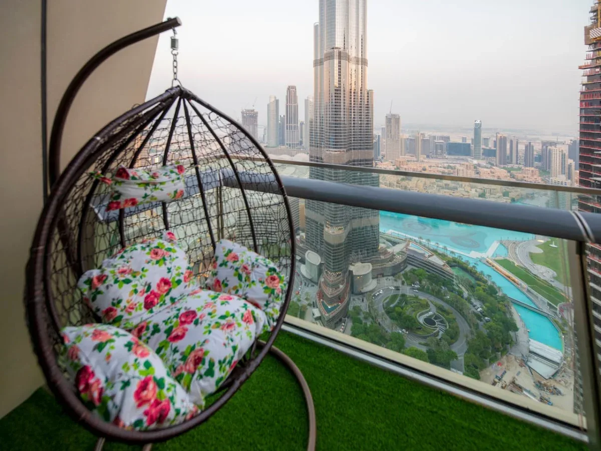 A balcony with a hanging chair overlooks a city skyline and turquoise water.