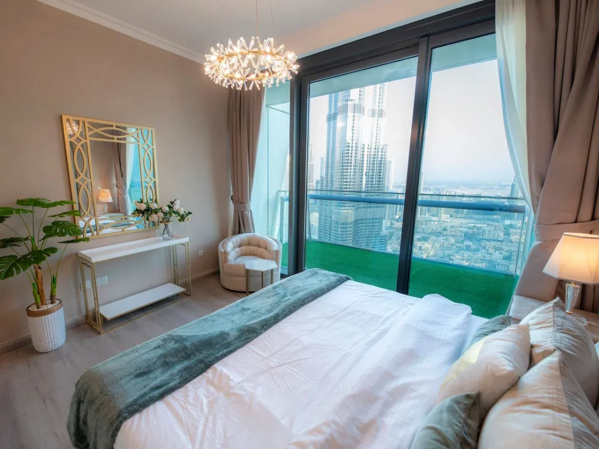 A bedroom with a bed beside floor-to-ceiling windows overlooking the city.