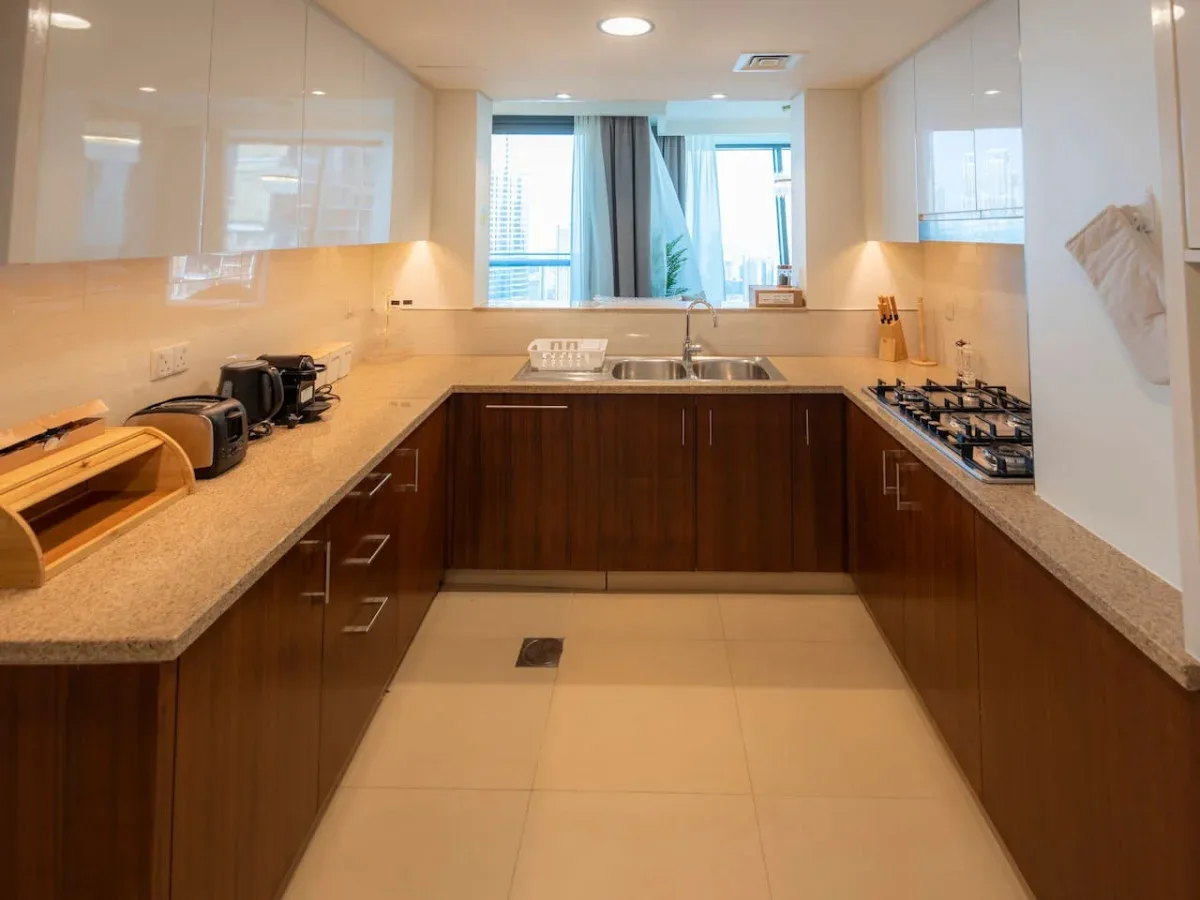 A modern kitchen with wood cabinets, light countertops, and a sink beneath the window.