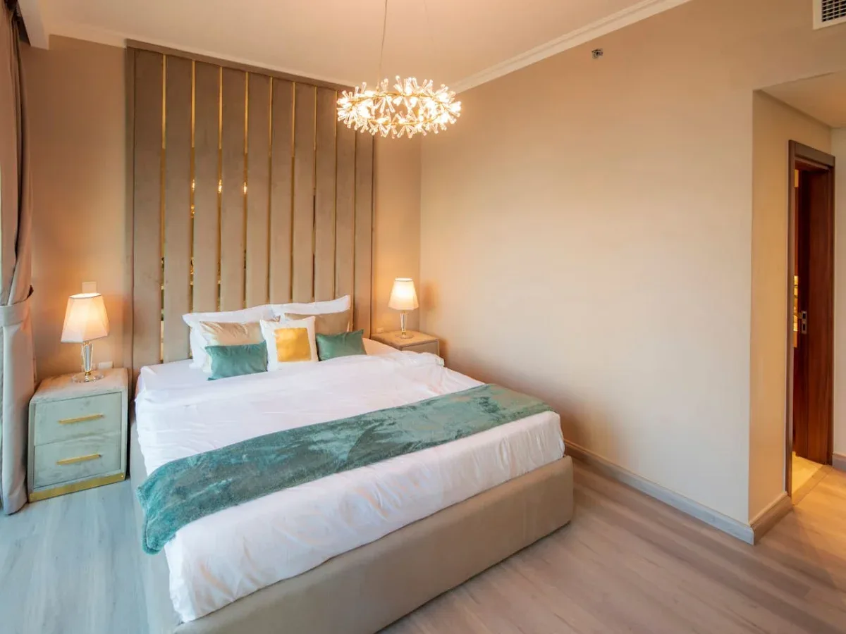 A bedroom with a bed dressed in white linens and a teal bed runner.