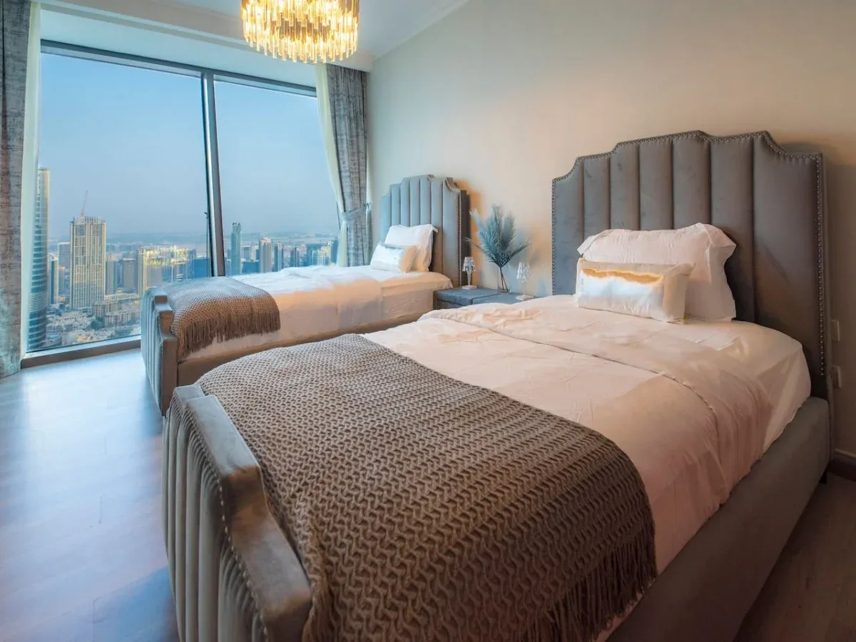 A bedroom with two beds beside a large window overlooking the city.