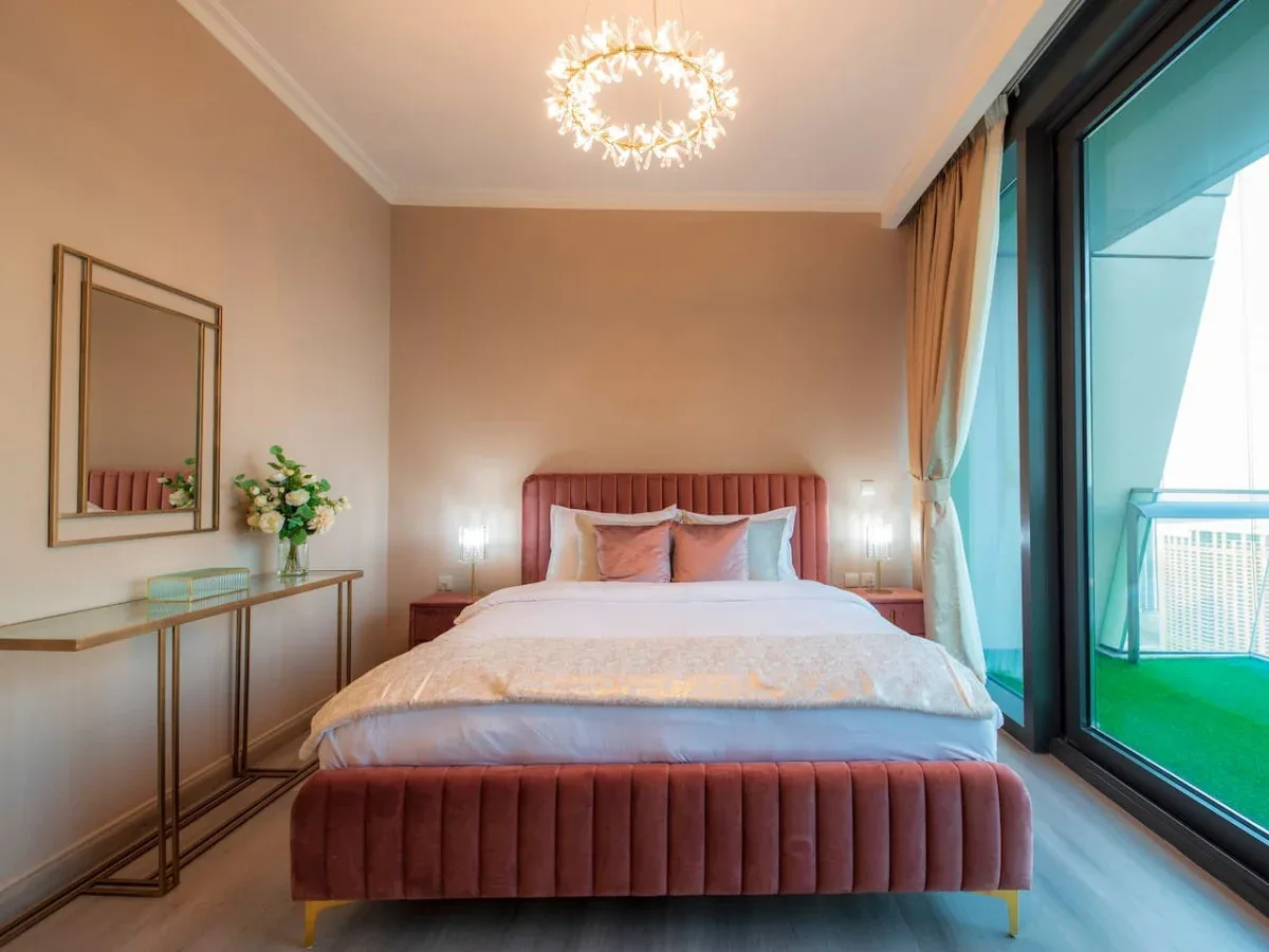 A bedroom with a bed, bedside tables, and large windows opening onto a balcony.