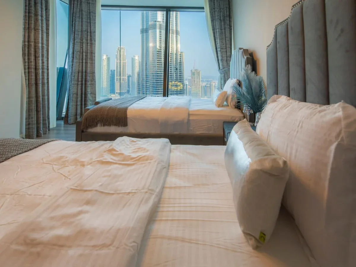A bedroom with two beds, a large window, and a city skyline view.
