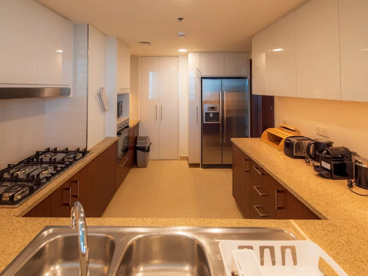 A modern kitchen with long countertops, a gas cooktop, and a stainless steel refrigerator.