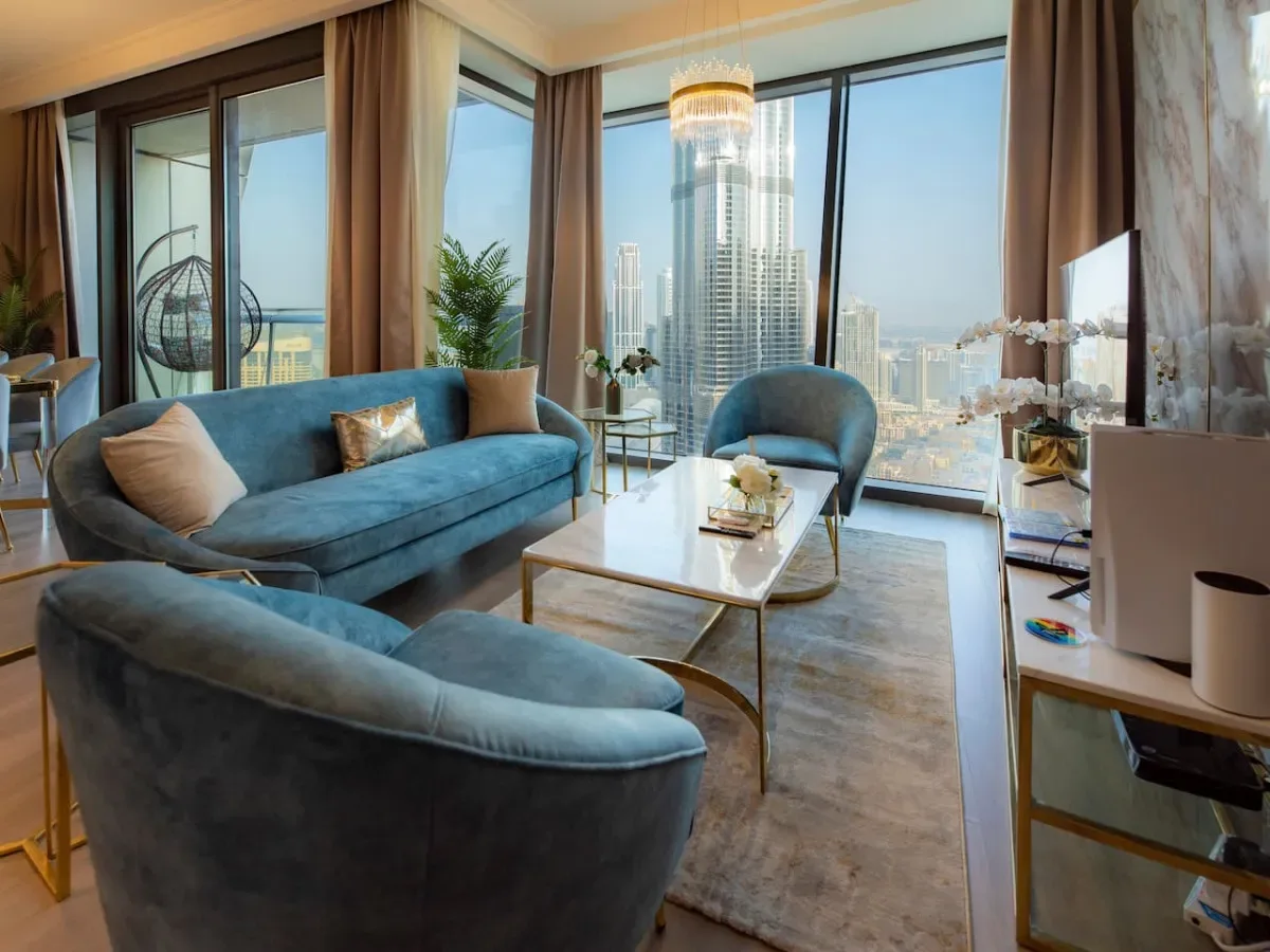 A living room with blue seating and floor-to-ceiling windows overlooking the city.