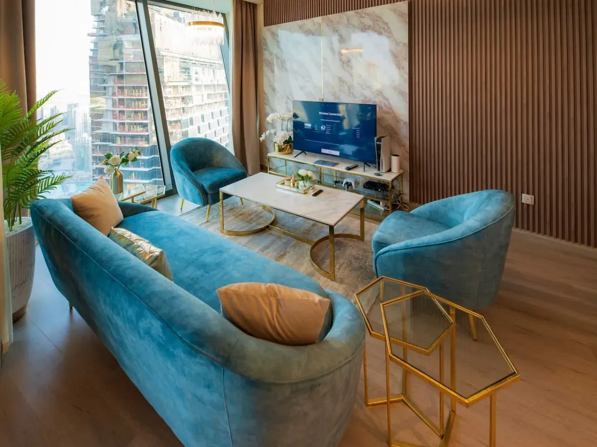 A living room with blue seating, a coffee table, and a television beside large windows.