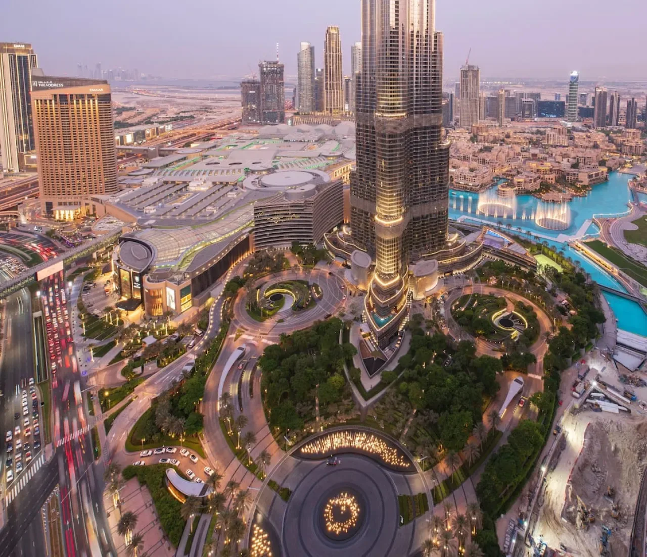An elevated cityscape shows a tall central tower, surrounding buildings, roads, and landscaped grounds.