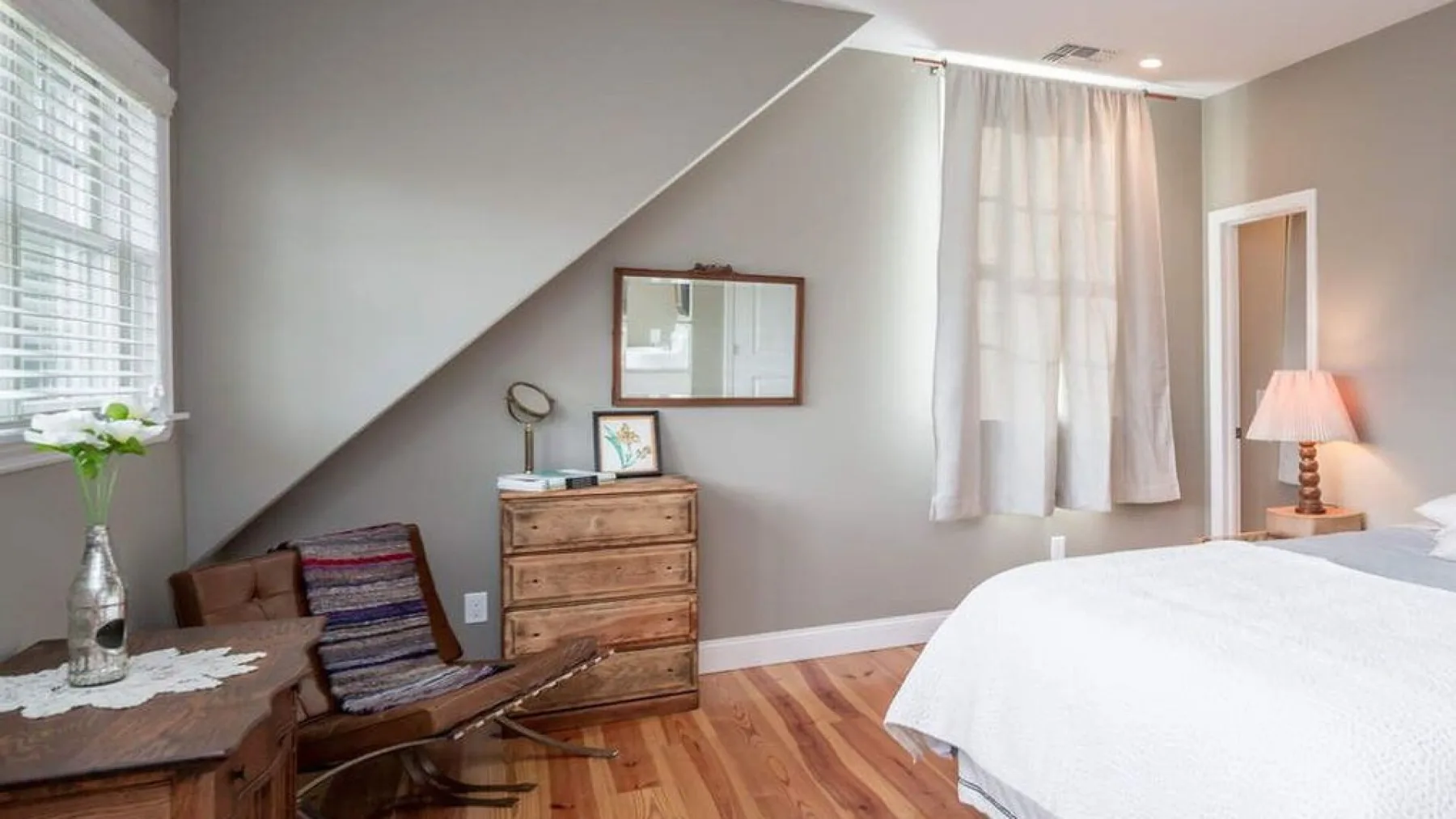 A bedroom with a neatly made bed, wooden flooring, and a dresser.