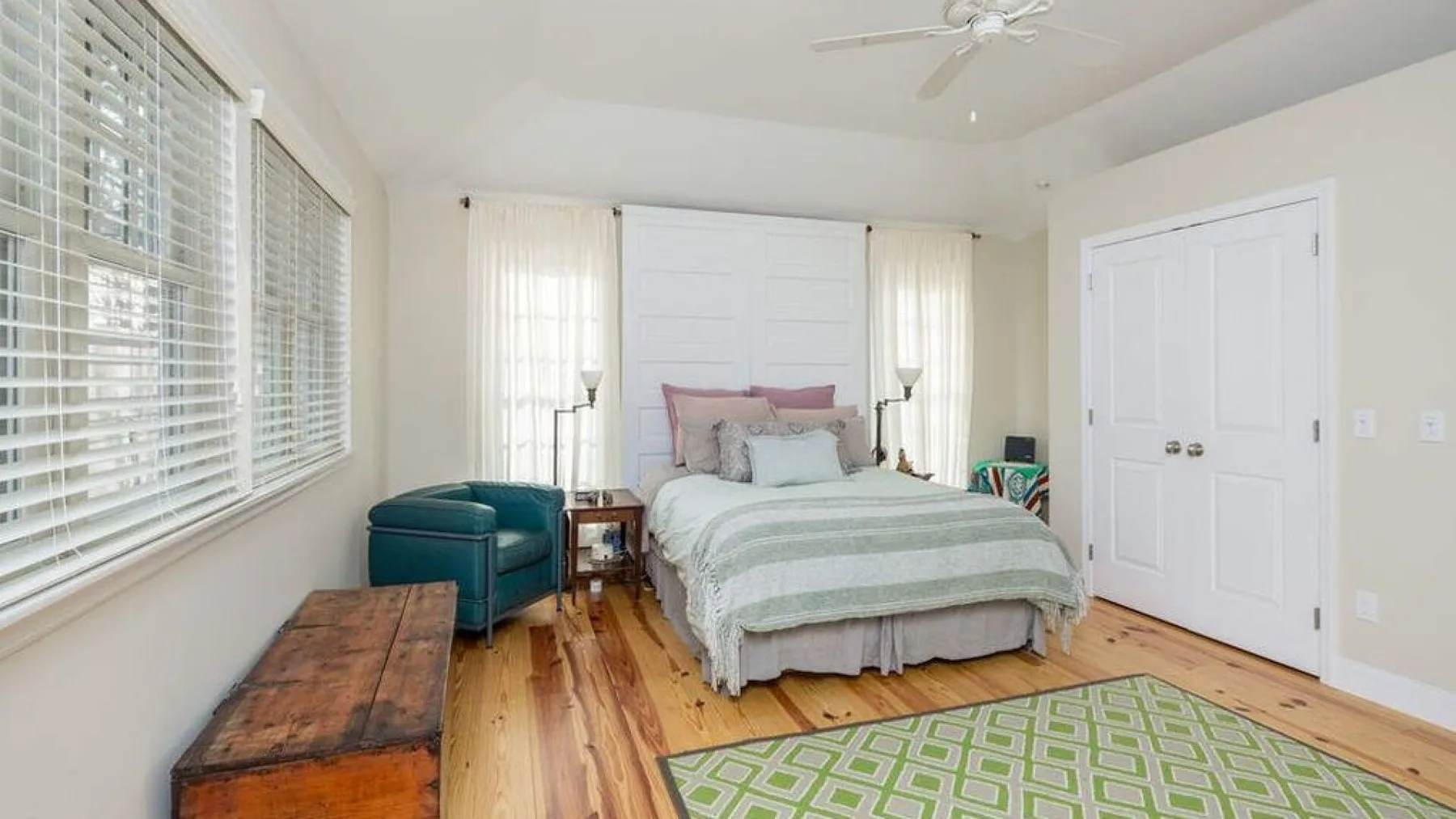 A bright bedroom has a bed, teal seating, and a green patterned rug.