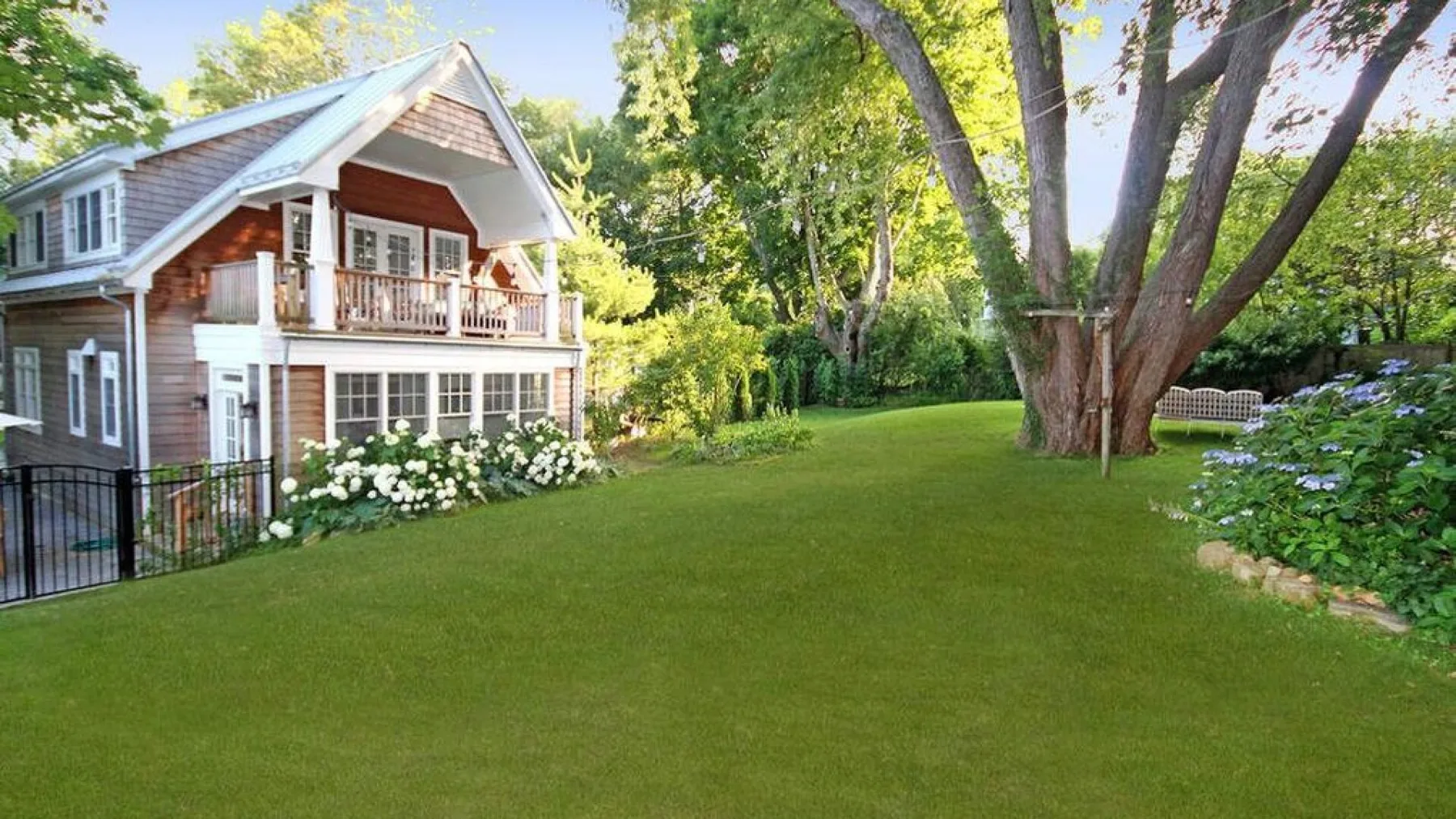 A house beside a broad green lawn, with mature trees and garden beds.