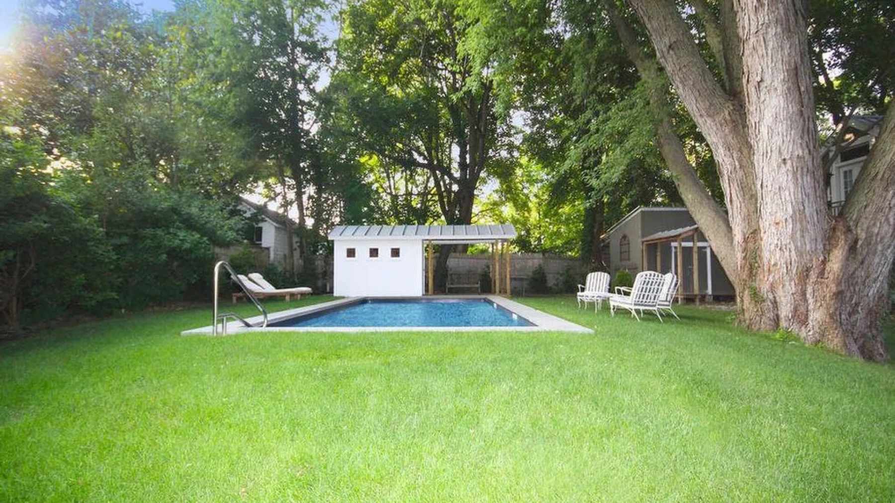 A backyard lawn surrounds a swimming pool, with trees and outdoor seating.