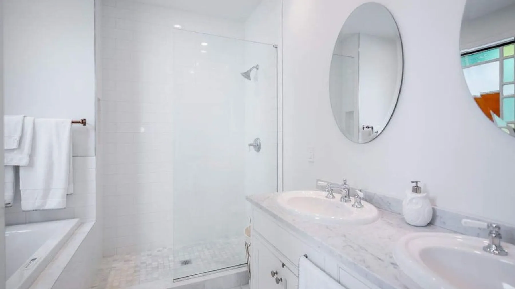 A bright bathroom with a glass shower, a long vanity, and two sinks.