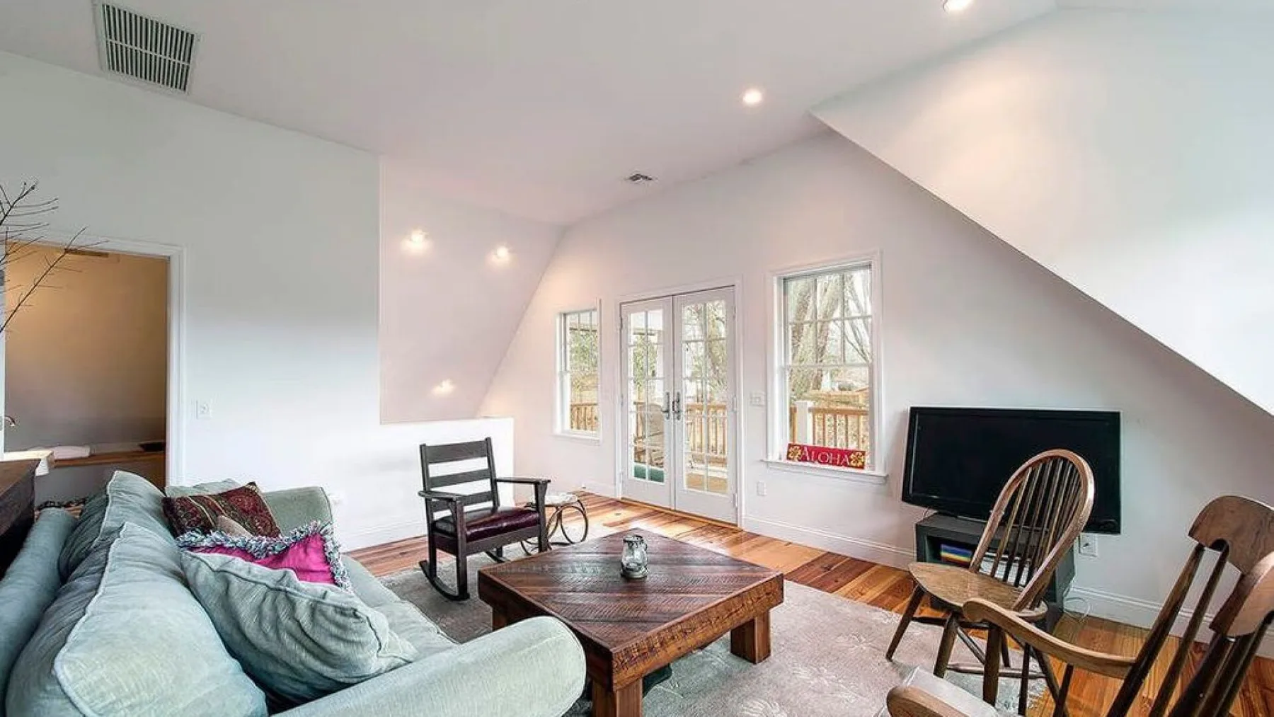 A bright living room has seating, a wooden coffee table, and windows beneath a sloped ceiling.