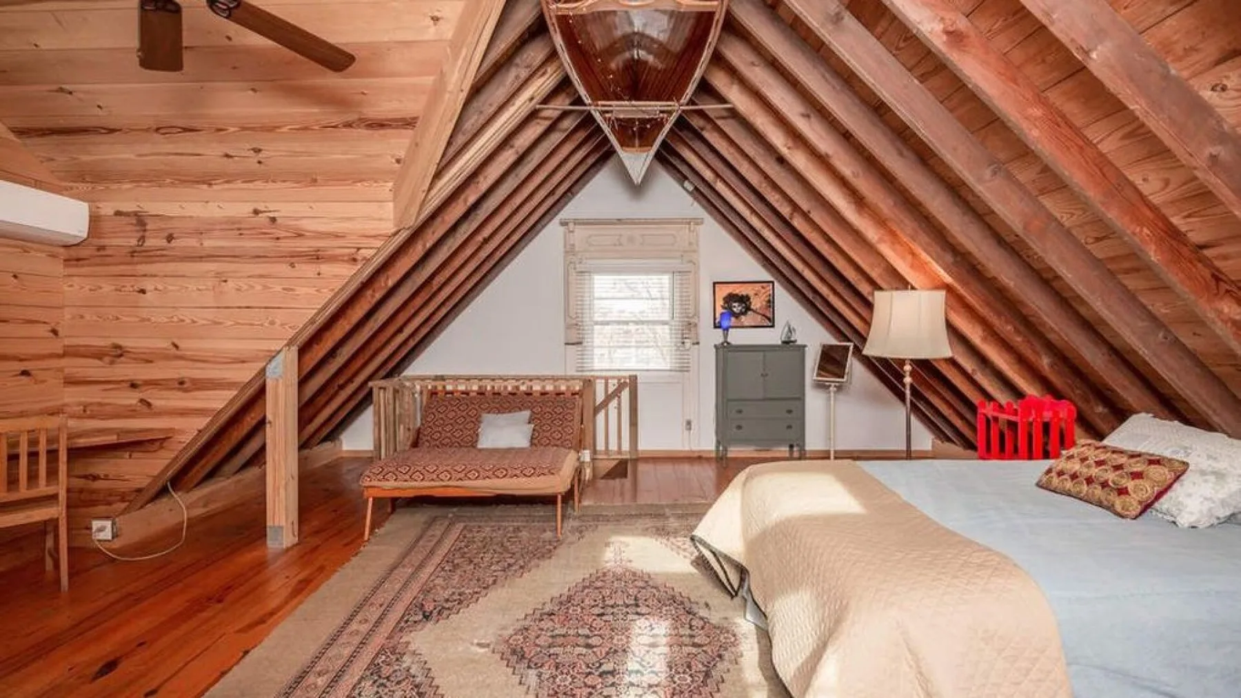A wood-paneled attic bedroom with a bed, seating, and a small window.