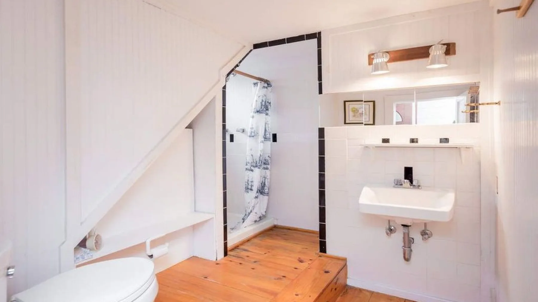A bathroom with a shower, sink, and sloped ceiling.