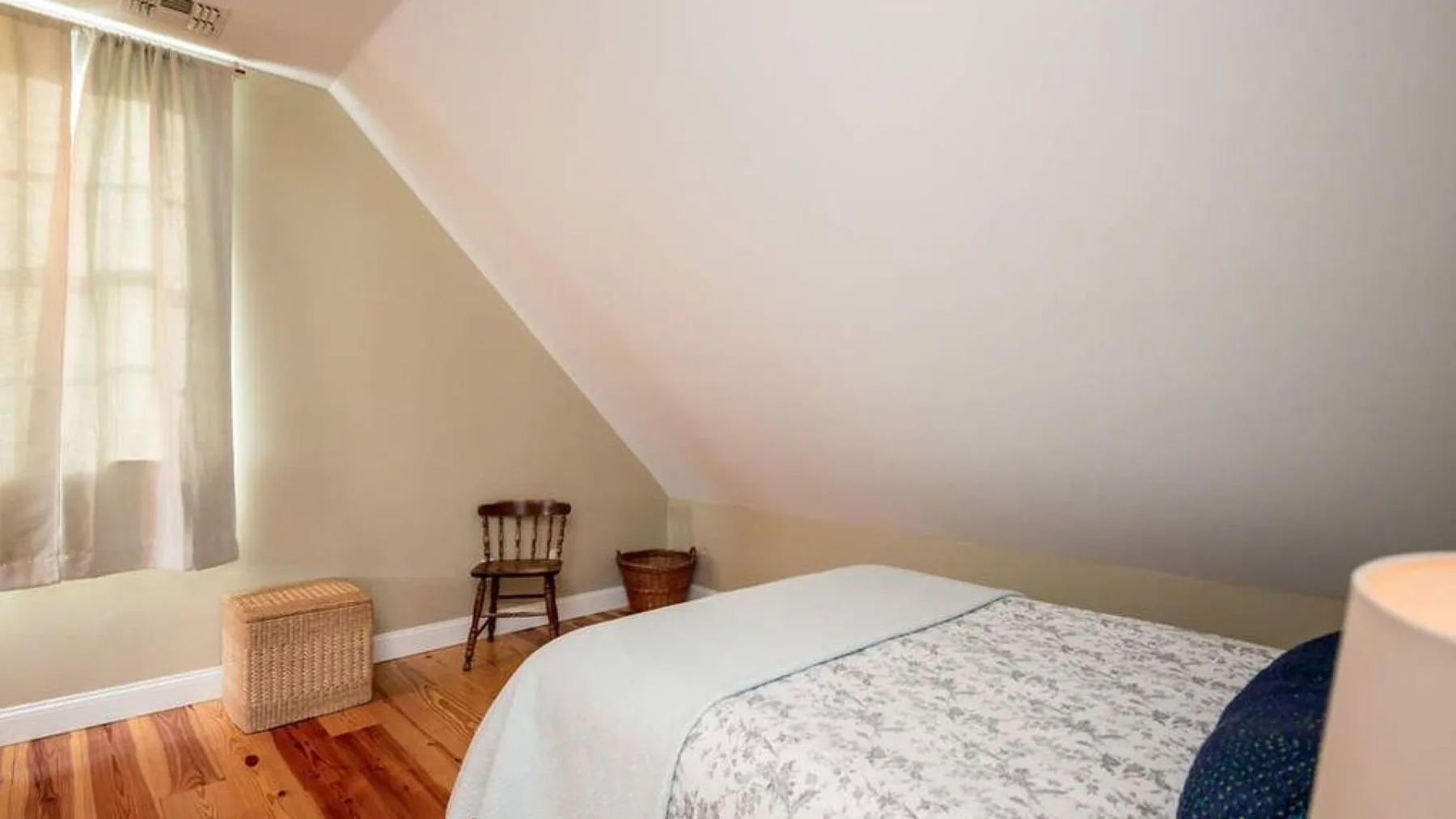 A bedroom with a bed, a curtained window, and a wooden floor.