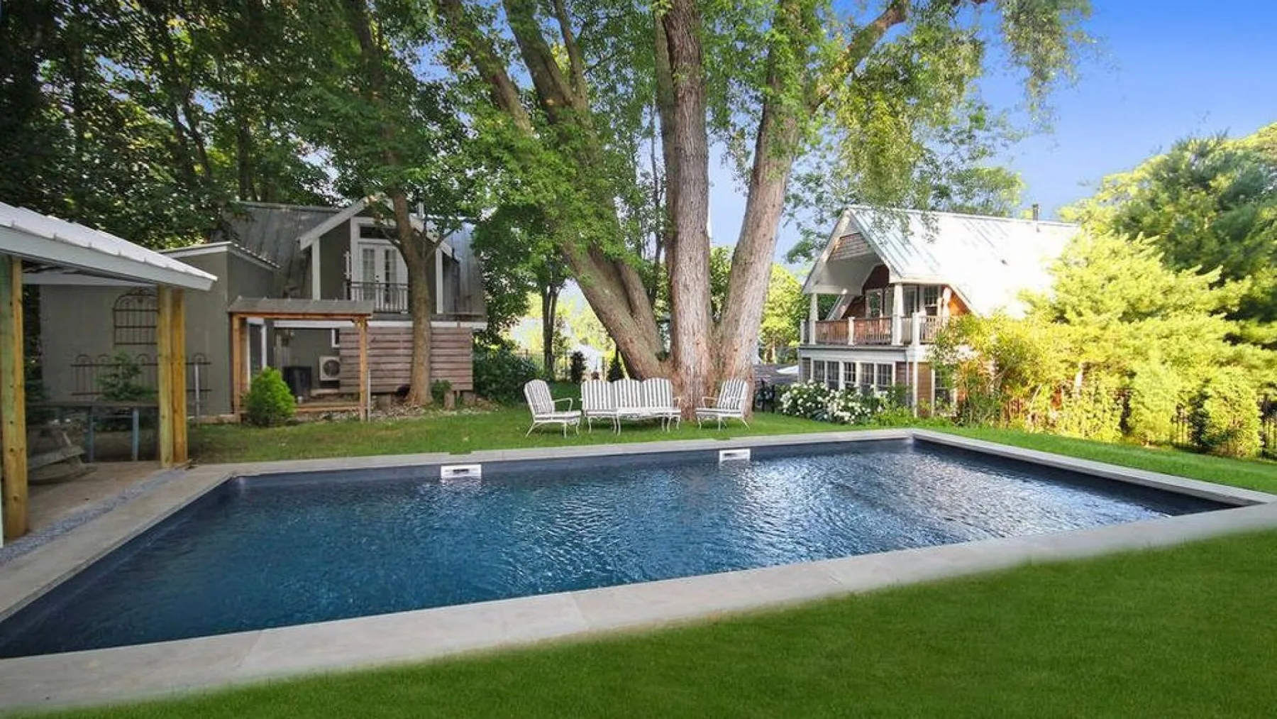 A swimming pool sits beside a lawn, with houses and trees in the background.