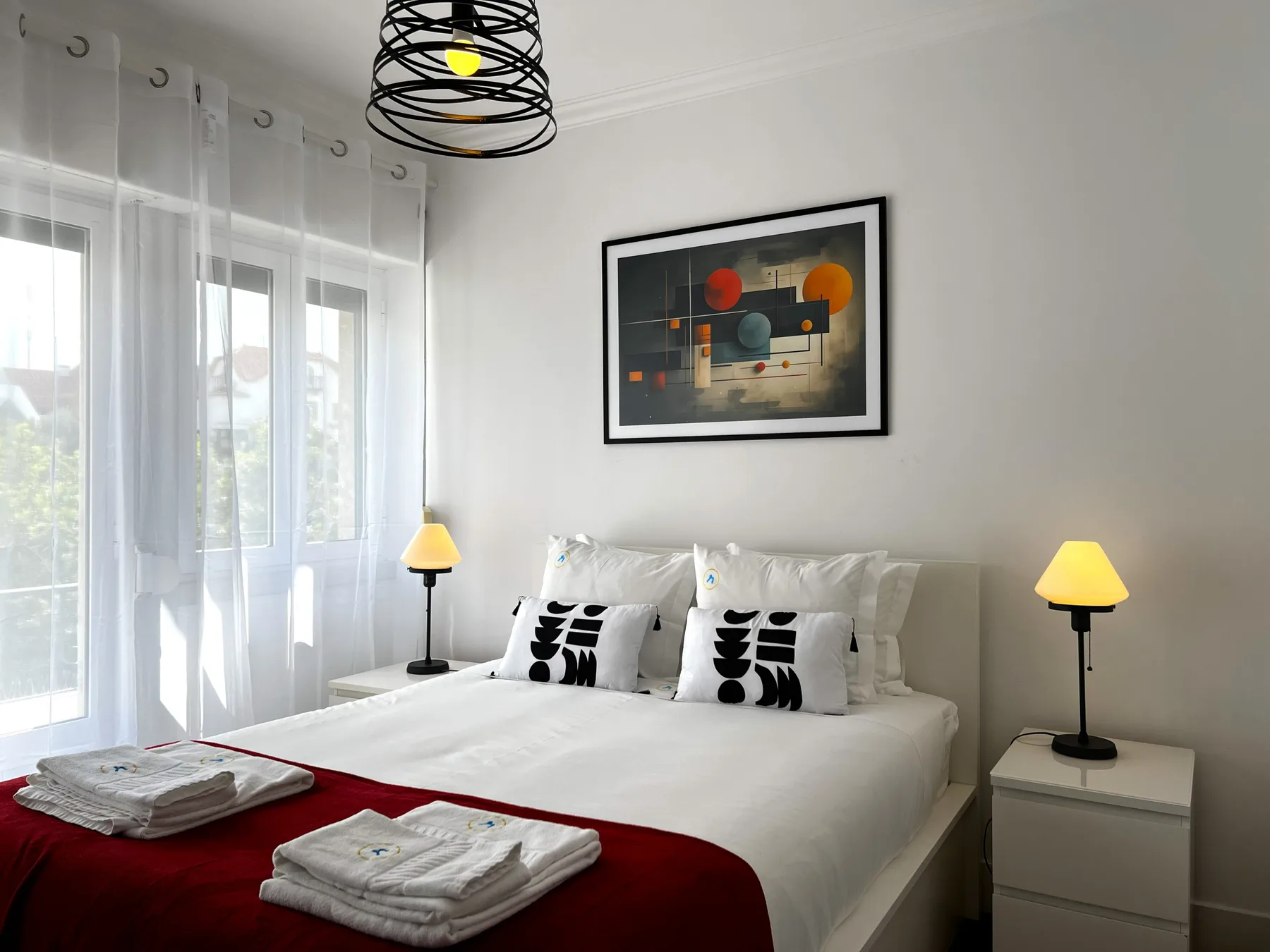 Un dormitorio luminoso con una cama doble, arte abstracto y cortinas translúcidas.