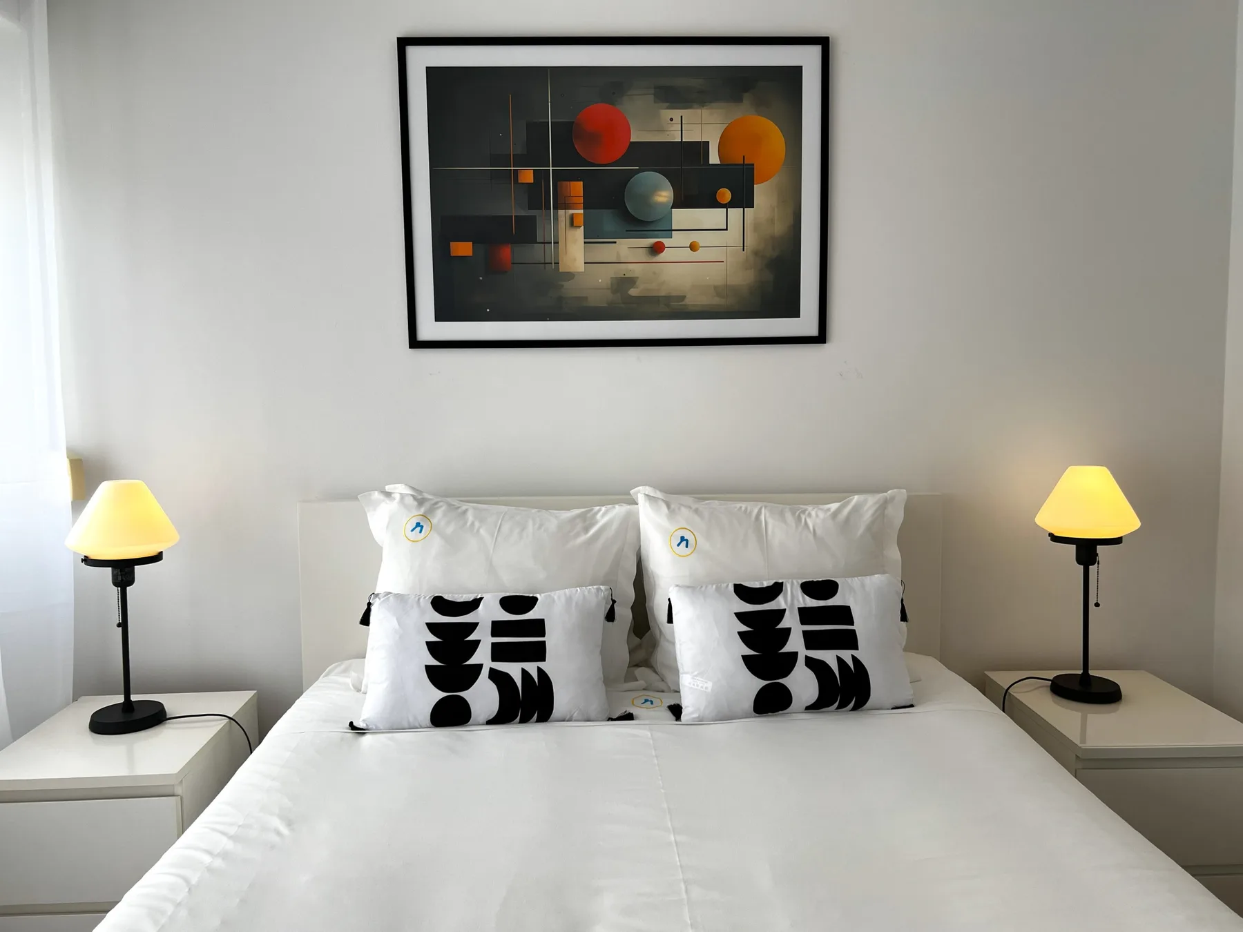 Un dormitorio con una cama bien tendida y una obra abstracta enmarcada encima.