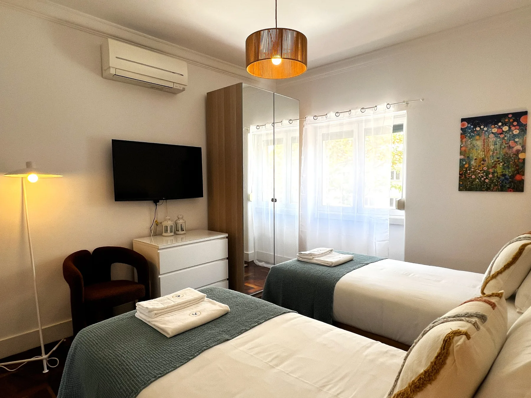 Un dormitorio con dos camas, una cómoda y una ventana con cortinas translúcidas.