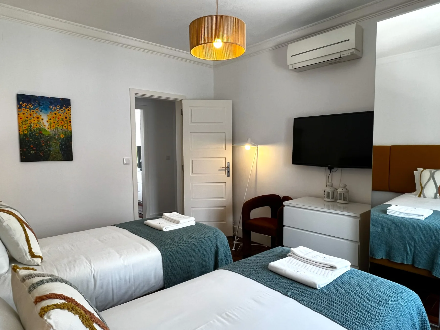 Un dormitorio con dos camas, mantas verde azulado y un televisor en la pared.
