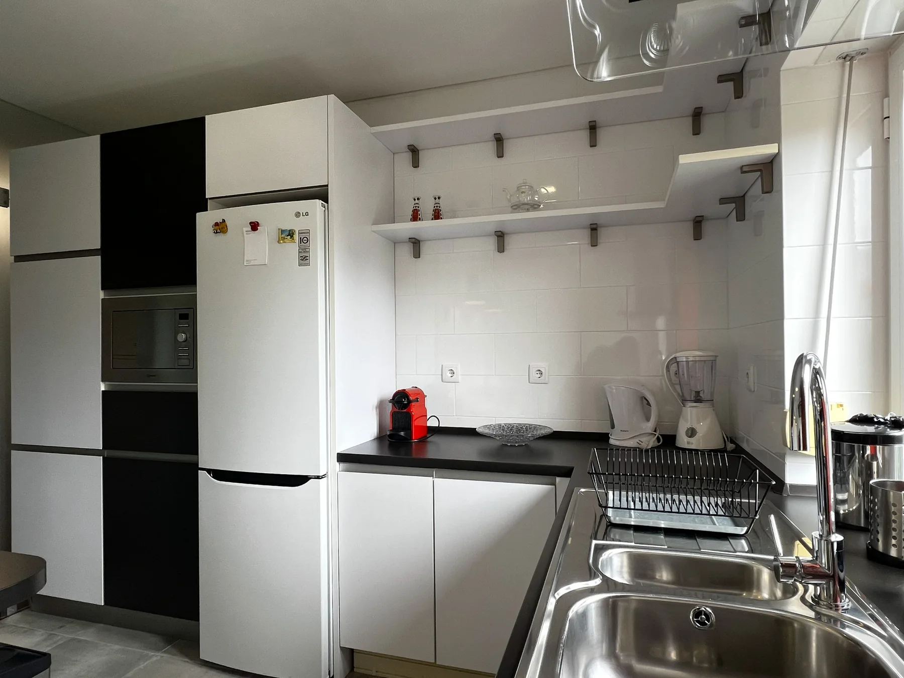 Una cocina luminosa con armarios blancos, un refrigerador y un fregadero doble.