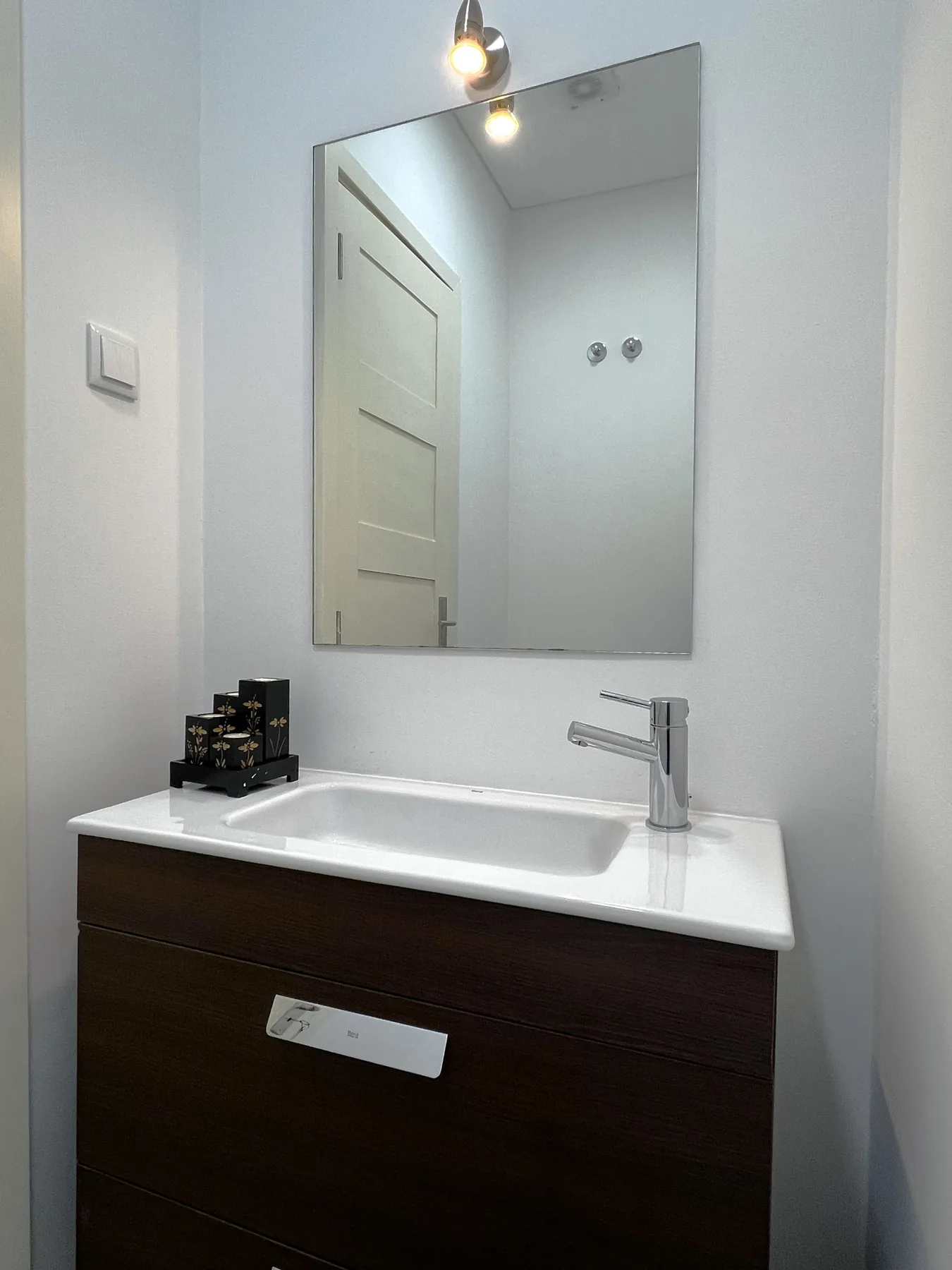 Un lavabo de baño compacto con un fregadero rectangular y un espejo de pared.