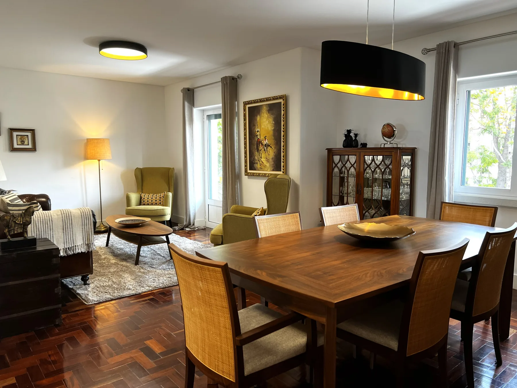 Sala de estar y comedor con una mesa de madera y asientos junto a grandes ventanas.