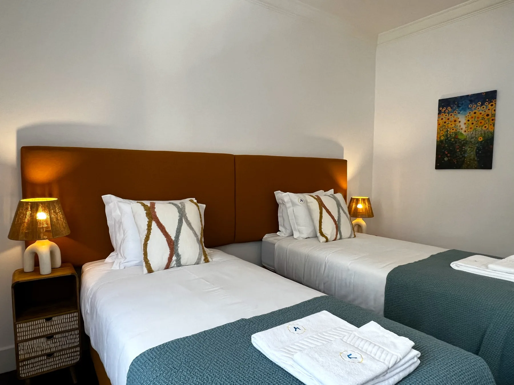 Un dormitorio con dos camas vestidas con sábanas blancas y cubrecamas verde azulado.