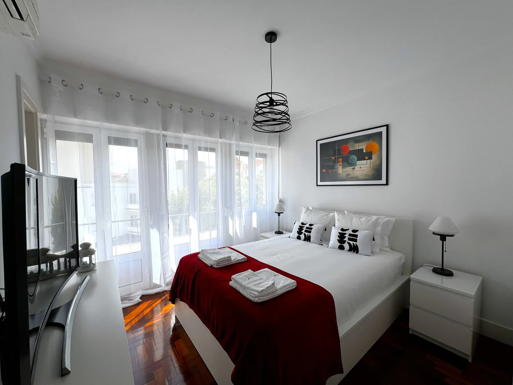 Un dormitorio luminoso con una cama doble, una colcha roja y puertas de cristal.