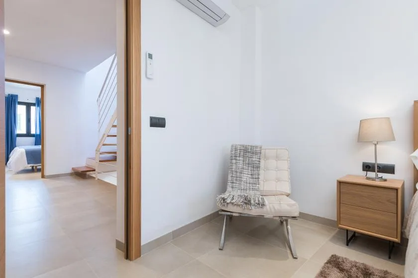 A bright room with a cushioned chair beside a wooden nightstand and lamp.