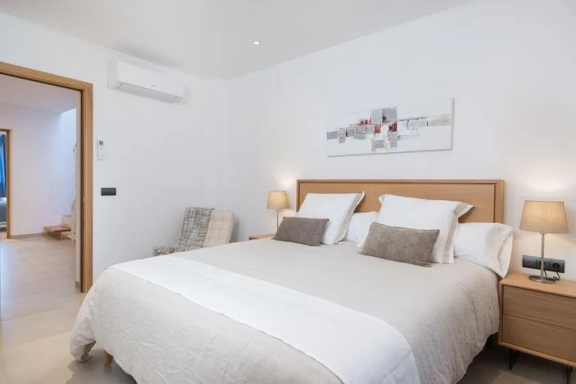 A bright bedroom features a neatly made bed and bedside lamps.