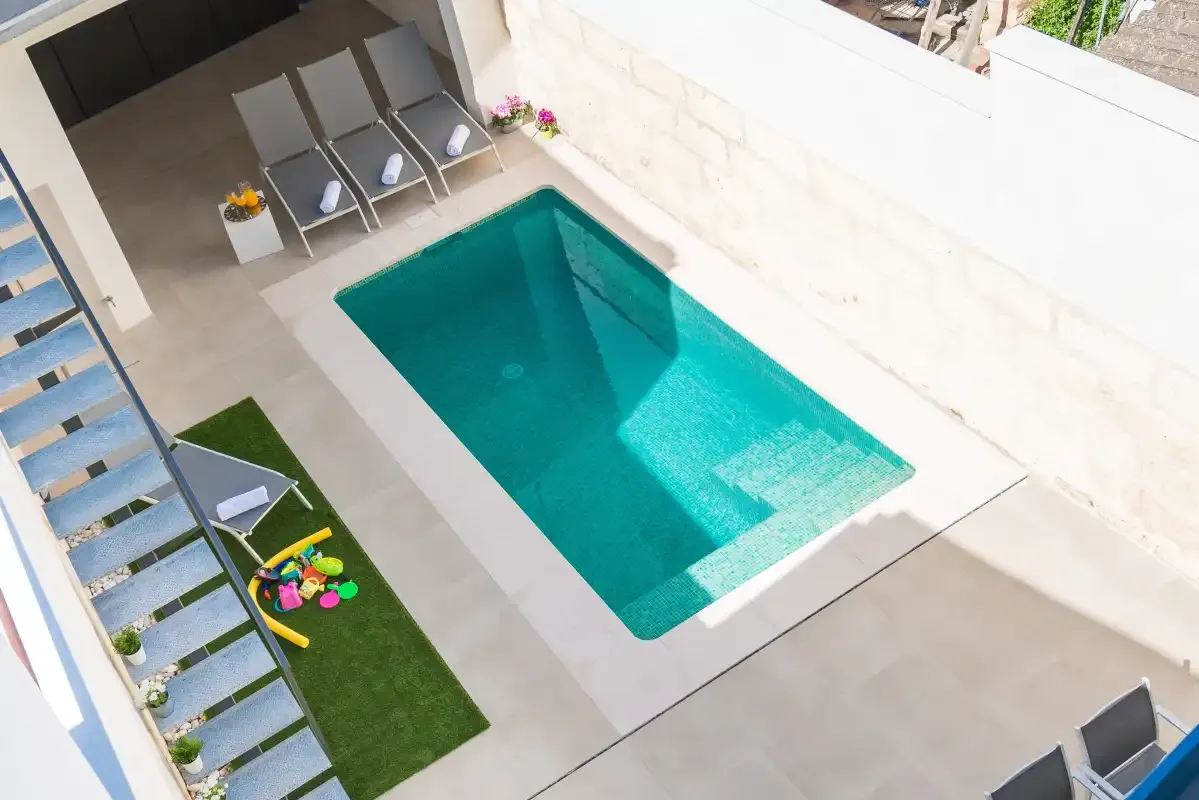A small outdoor swimming pool is surrounded by paved space and lounge seating.
