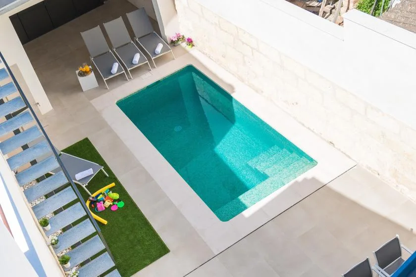 A small outdoor pool sits beside a paved patio with lounge seating.