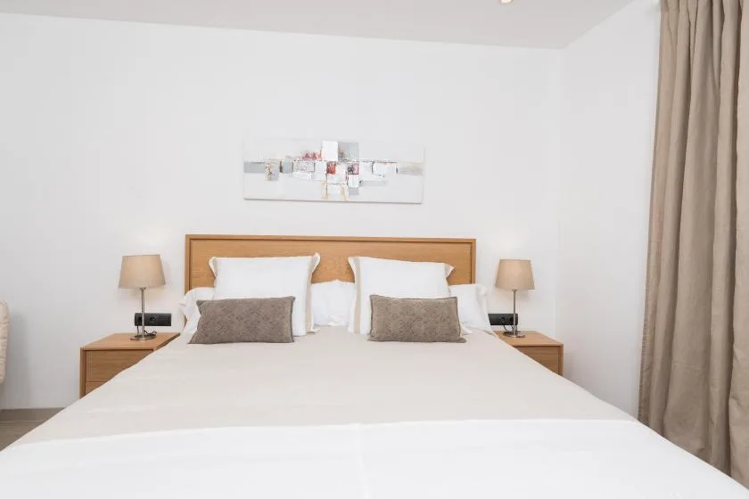 A bedroom with a neatly made bed, bedside tables, and curtains.