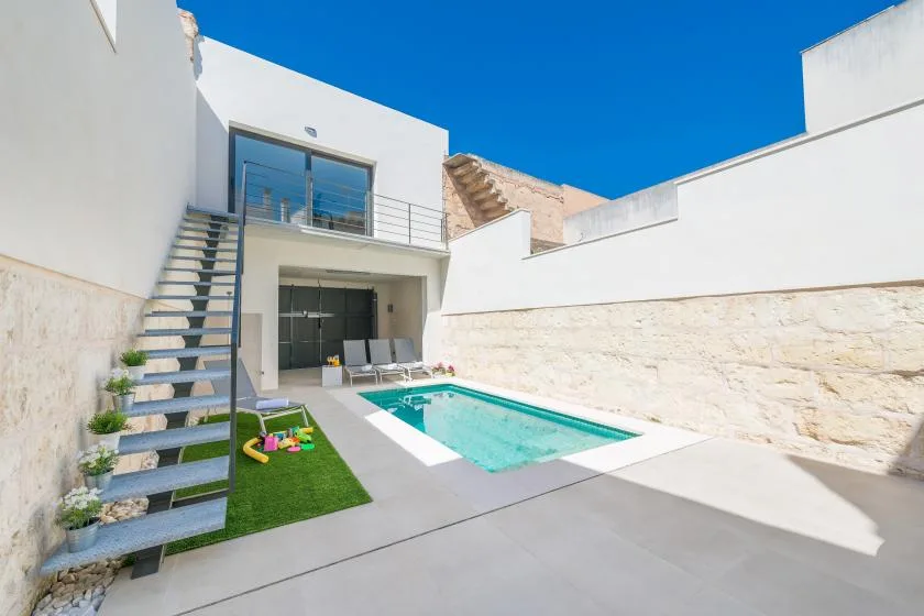 A courtyard pool sits beside a modern white building and a small patch of artificial grass.