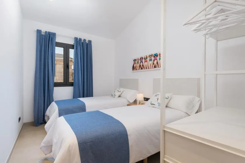 A bright bedroom with white bedding, blue runners, and blue curtains beside the window.