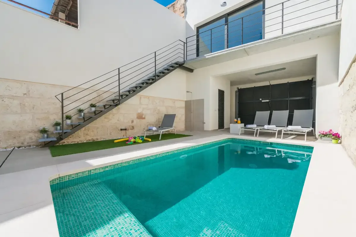 A courtyard pool sits beside a modern white building and outdoor seating.