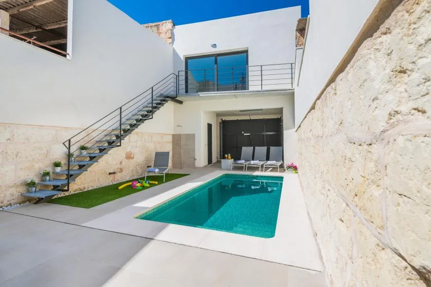 A courtyard pool sits beneath an outdoor staircase beside a modern white building.
