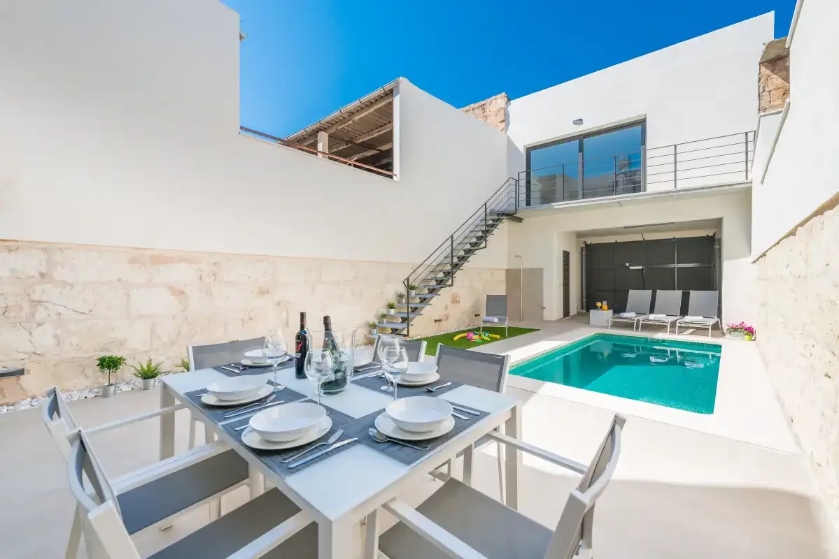 Outdoor dining area beside a swimming pool in a bright courtyard.