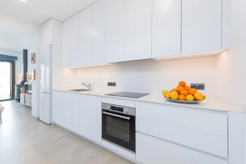 A bright modern kitchen with white cabinets and fruit on the counter.